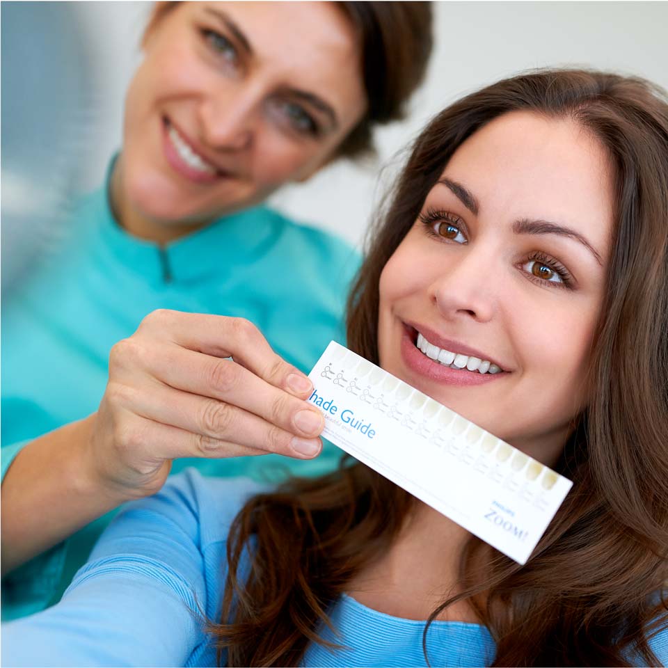 A dental professional holding a teeth shade guide in front of a patient's smile