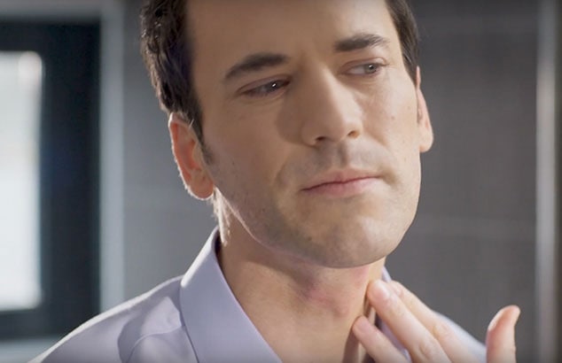 A clean-shaven man placing his fingers against some red bumps after shaving on his neck.