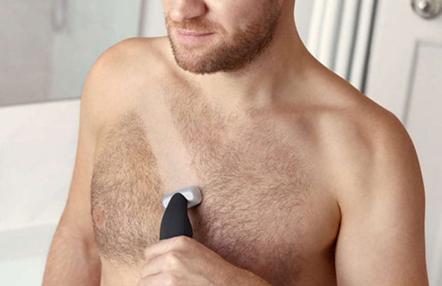 : Close-up of a man’s hairy chest with stripe being shaven across by an electric shaver he is holding.