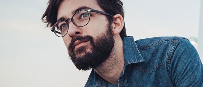 A dark-haired man in denim shirt with a thick beard.