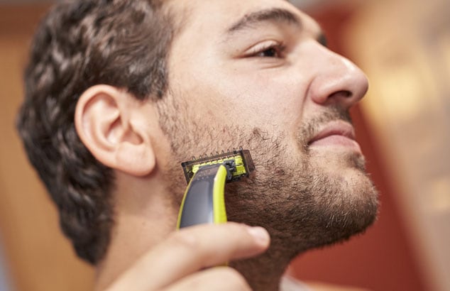 A man is trimming his short chin beard using a trimmer with a special attachment.