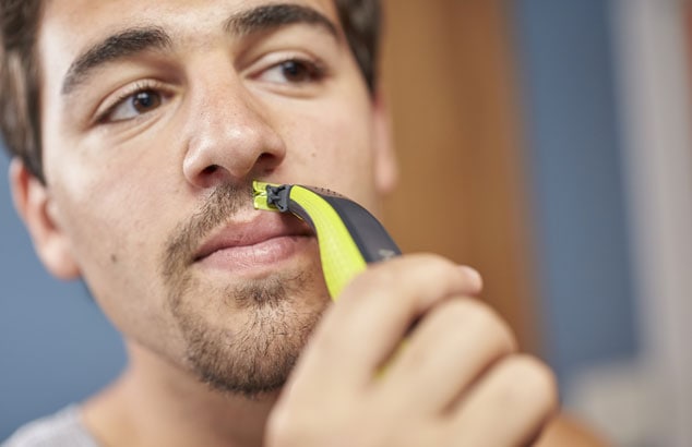 Man with brown hair and eyes using Philips OneBlade to shape his goatee chin beard above his lips.