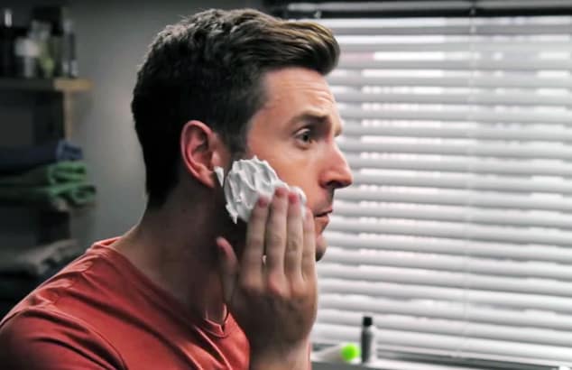 Man applying shaving foam onto his face in a bathroom.