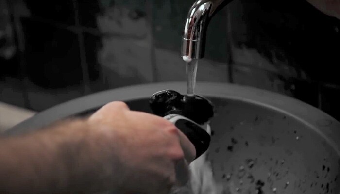 Rinsing shaver with water under a tap to clean before use